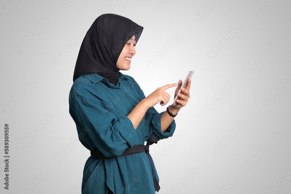 Portrait of excited Asian muslim woman with hijab holding and touching mobile phone. Advertising concept. Isolated image on white background Portrait of excited Asian muslim woman with hijab holding and touching mobile phone. Advertising concept. Isolated image on white background