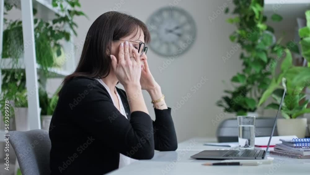 Mature woman drinking pill while sitting at her desk in home office Mature woman drinking pill while sitting at her desk in home office