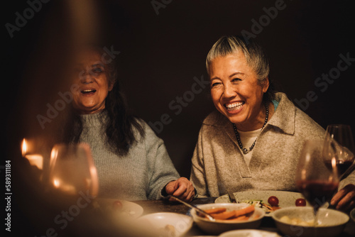 Happy senior woman laughing by female friend at dinner party