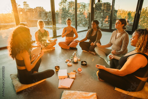 Multiracial female friends meditating together sitting cross-legged at retreat center