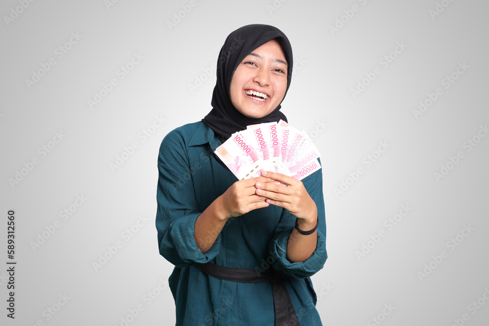 Portrait of excited Asian hijab woman in casual outfit showing one hundred thousand rupiah. Financial and savings concept. Isolated image on white background Portrait of excited Asian hijab woman in casual outfit showing one hundred thousand rupiah. Financial and savings concept. Isolated image on white background
