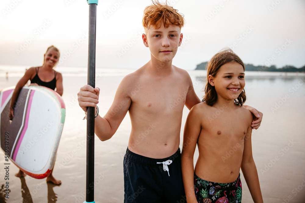 Portrait of shirtless boy with arm around sister at beach during