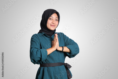 Portrait of cheerful Asian woman hijab in casual shirt, showing apologize and welcome hand gesture. Advertising concept. Isolated image on white background photo