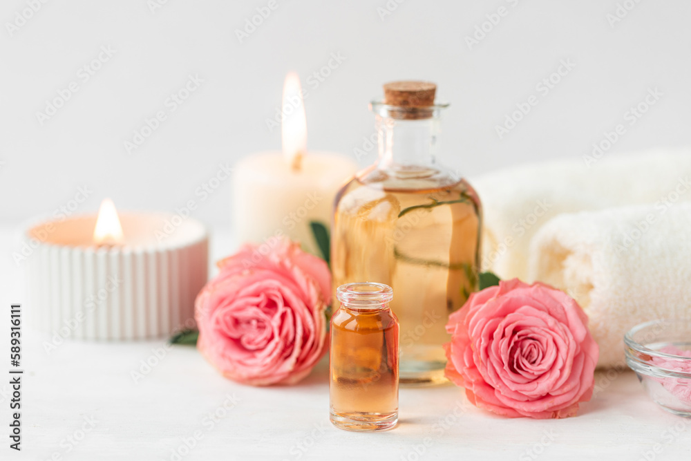 Aromatherapy. Concept of pure organic essential rose oil. Elixir with plant based floral or herbal ingredients. Pink flowers extract. Spa atmosphere with candle, towel. White background Aromatherapy. Concept of pure organic essential rose oil. Elixir with plant based floral or herbal ingredients. Pink flowers extract. Spa atmosphere with candle, towel. White background