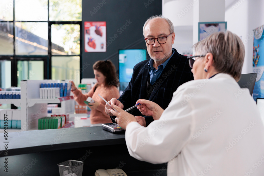 Obraz premium Elderly pharmacist standing at drugstore counter looking at client health care prescription, helping him with pharmaceutics treatment working in pharmacy. People shopping for vitamins, supplements