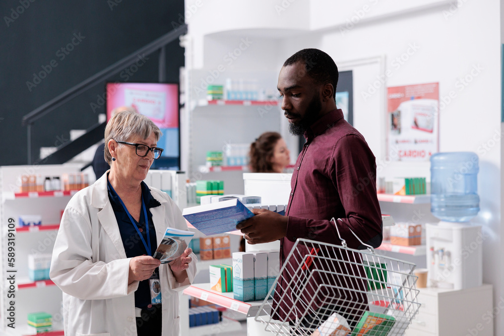 African american client discussing with pharmacist asking for help with cardiology drugs, worker explaining medical leaflet. Drugstore employee offering support assistance, medicine service