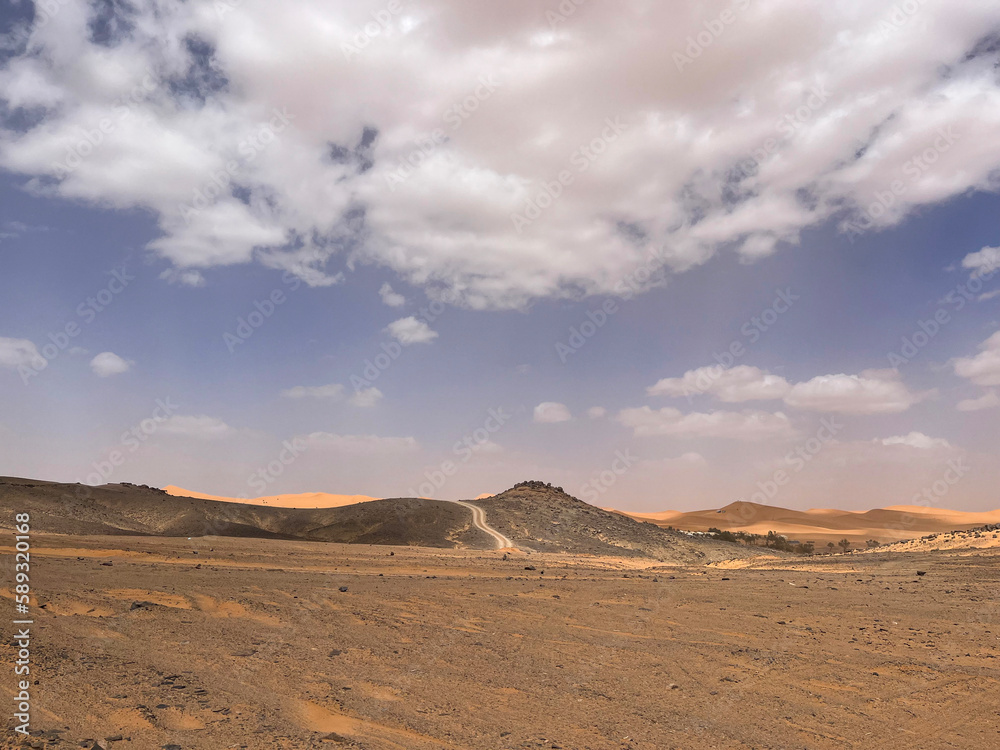 Merzouga, Morocco, Africa, panoramic road in the Sahara desert in the Black Mountain area, with view of the black stones, fossils and sand dunes, 4x4 trip, blue sky and white clouds