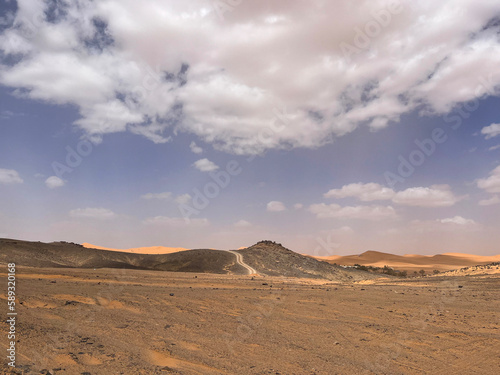 Merzouga, Morocco, Africa, panoramic road in the Sahara desert in the Black Mountain area, with view of the black stones, fossils and sand dunes, 4x4 trip, blue sky and white clouds