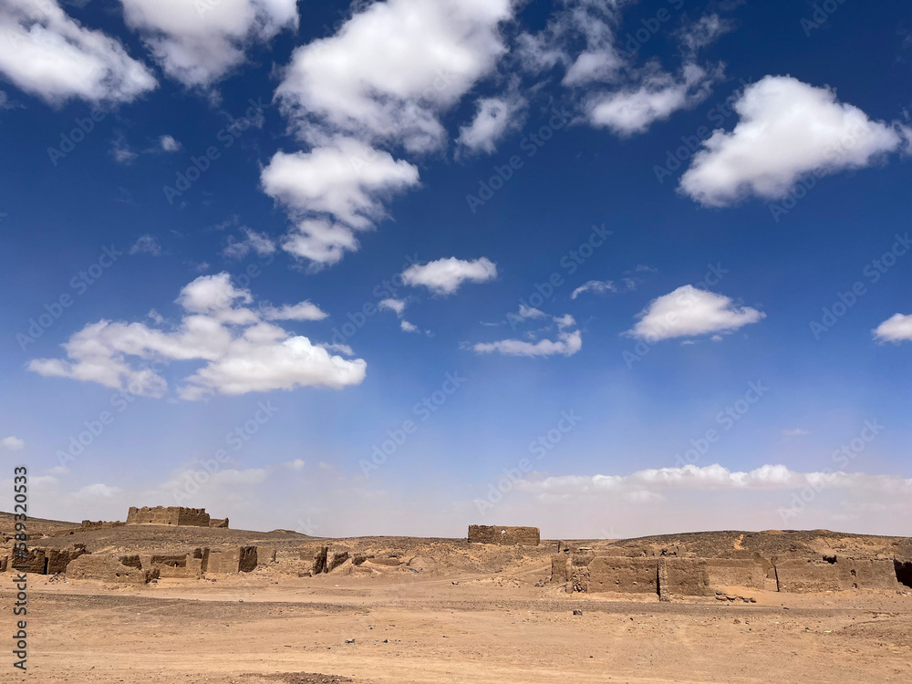 Merzouga, Morocco, Africa, panoramic road in the Sahara desert, ruined houses in an ancient and abandoned nomadic village, near the fossil mines in the Black Mountain area, blue sky and white clouds
