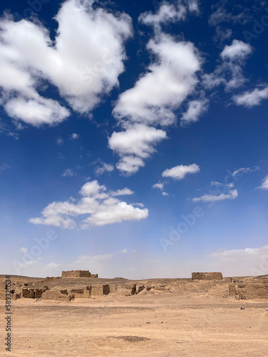Merzouga, Morocco, Africa, panoramic road in the Sahara desert, ruined houses in an ancient and abandoned nomadic village, near the fossil mines in the Black Mountain area, blue sky and white clouds
