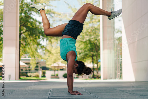 mujer morena con ropa urbana practicando capoeira en la ciudad y haciendo flexiones photo