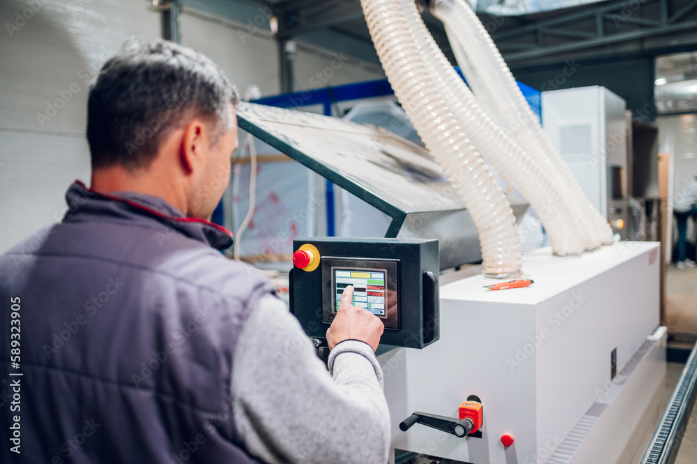 Back view of a carpenter operating a wood processing machine at the facility. Back view of a carpenter operating a wood processing machine at the facility.