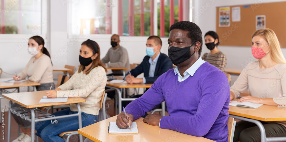 Fototapeta premium African-american student wearing protective mask among students in university classroom