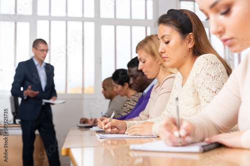 Concentrated hispanic girl attentively listening and making notes of lecture during adult education class