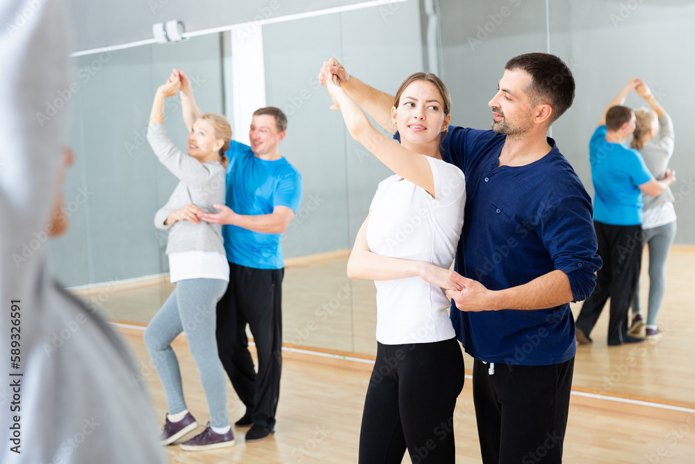 Smiling dancing people practicing bachata movements in dance studio for adults