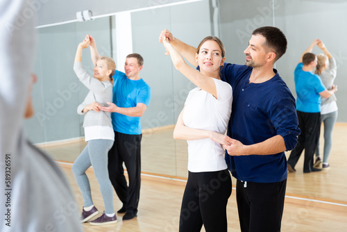 Smiling dancing people practicing bachata movements in dance studio for adults