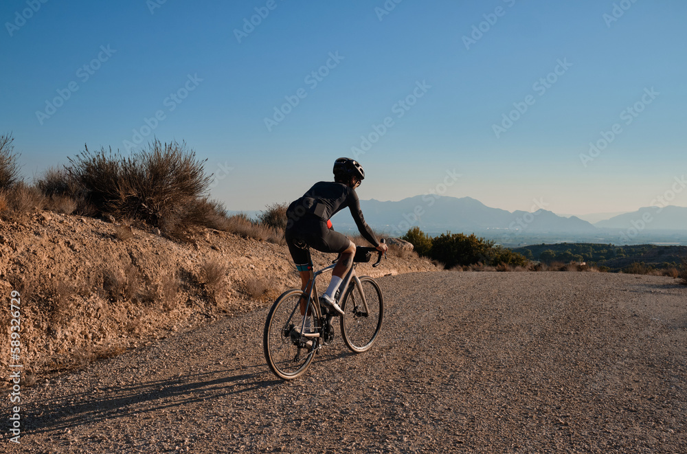 Fit male cyclist riding dirt trails on gravel bike. Man riding gravel bike on gravel road in scenic view with hills in Spain. Sport motivation.Gravel road in mountains. Fit male cyclist riding dirt trails on gravel bike. Man riding gravel bike on gravel road in scenic view with hills in Spain. Sport motivation.Gravel road in mountains.
