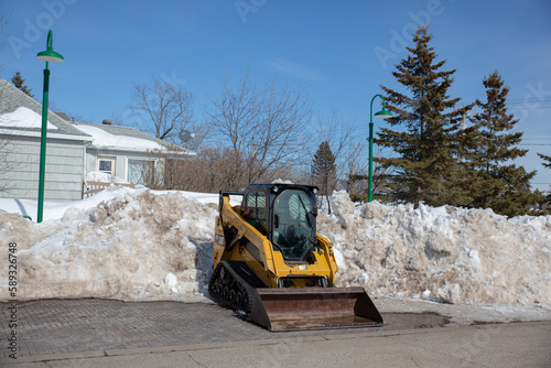 A bobcat steer loader in front of a snow bank.