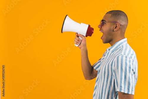 young Afro-American man announcing discounts in a megaphone, orange background medium shot, sales concept. High quality photo