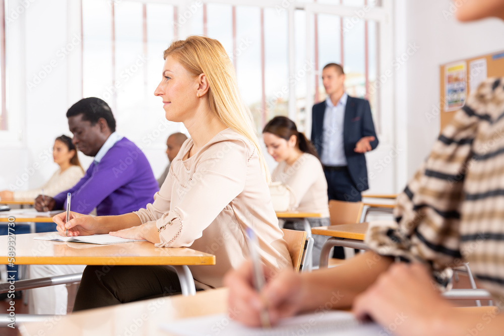 Obraz premium Cheerful woman listening lecture with interest and taking notes during adult education class..