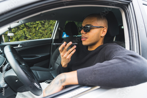 attractive young man sitting in a car recording a voice message to send, medium shot outdoors. High quality photo © PoppyPix