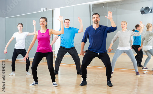 Fototapeta Naklejka Na Ścianę i Meble -  Group of sporty people doing stretching exercises before dance training in modern studio