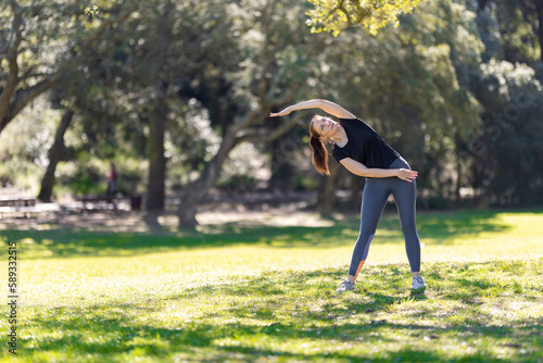 An adult woman in sports doing fitness exercise in the park