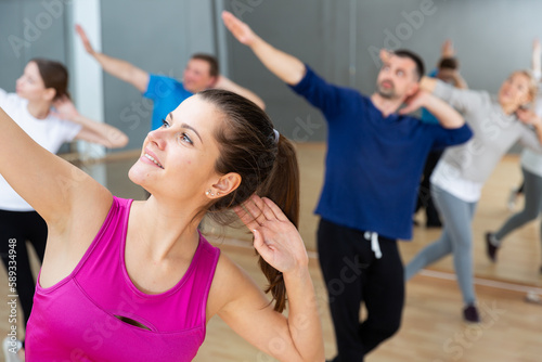 Smiling young female coach doing dance workout with adult group in fitness center