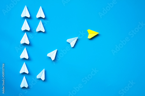 Yellow paper airplane origami leaving with other white airplanes on blue background with customizable space for text or ideas. Leadership skills concept and copy space for text