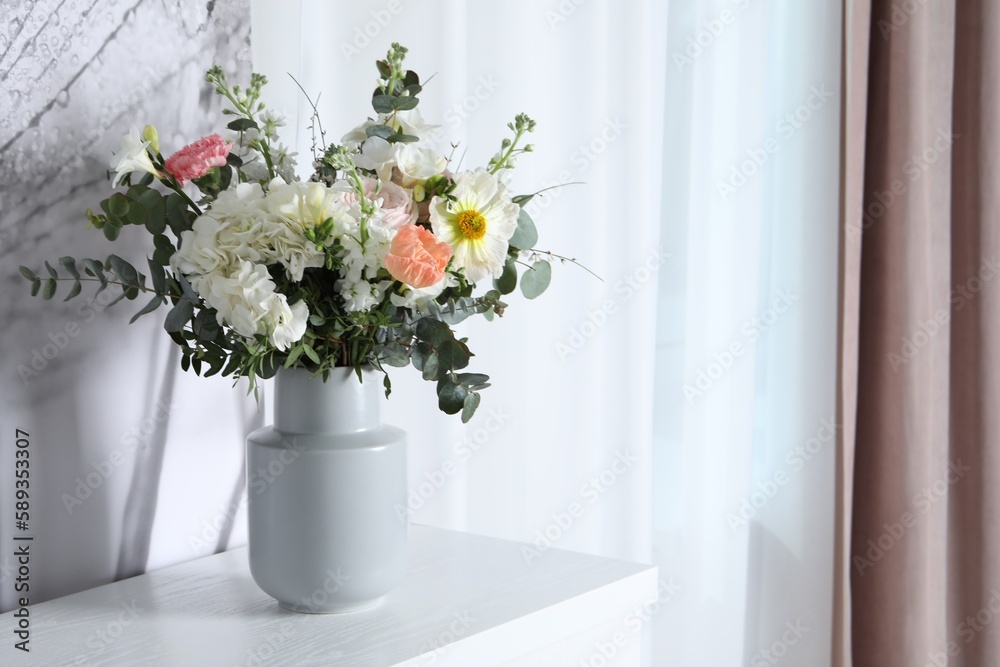 Bouquet with beautiful flowers on white chest of drawers indoors. Space for text