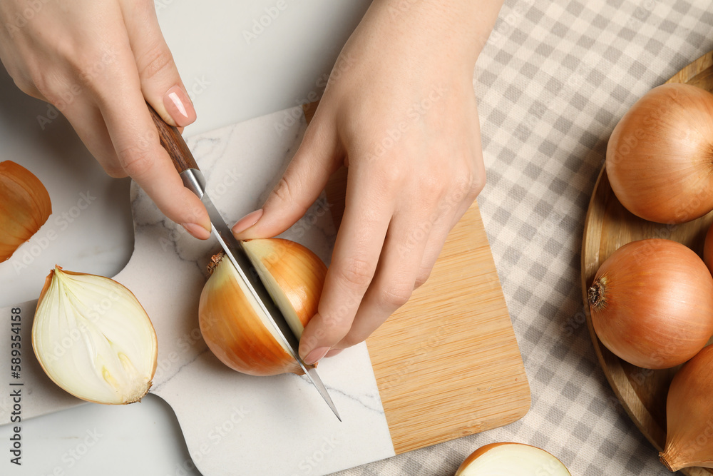 Obraz premium Woman cutting ripe onion at white marble table, top view