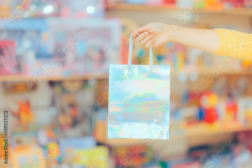 Customer Hand Holding a Holographic Shopping Bag in a Store. Client holding a gift bag buying present in sale season
 photo