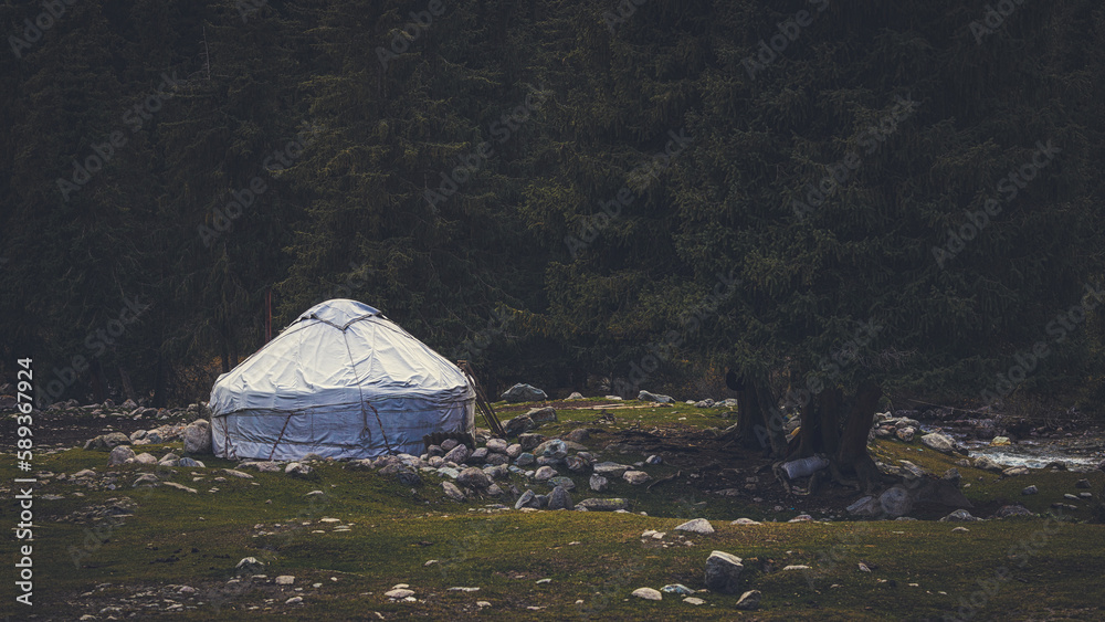 Traditional yurt house surrounded by beautiful coniferous forest and mountains in autumn, Kyrgyzstan