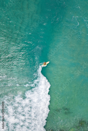 Surfer in the blue transparent ocean in Hawaii from above, aerial drone shot. © Nikita