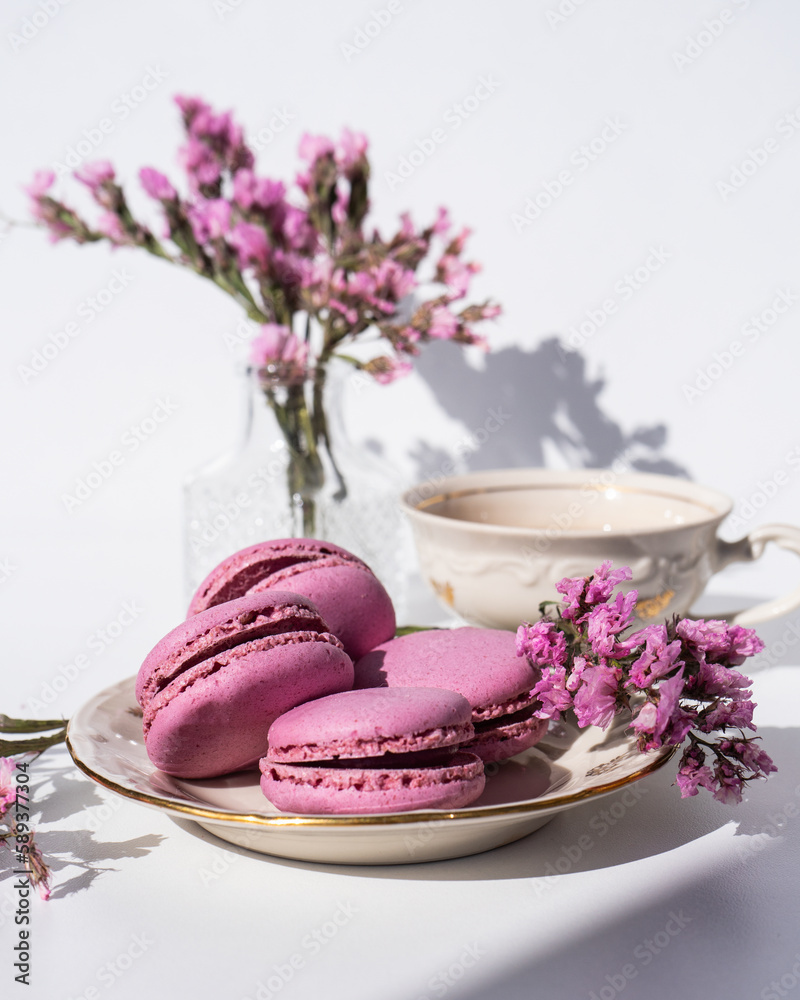 A cup of tea with almond cookies on a white background. Pink pasta and a mug. Flowers in a vase. Macaroons. A Cup of Tea. A white cup and pink macaroons on a white table. Selective focus.