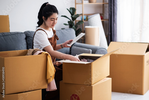 New house, asian woman check list of stuff in the box while feeling proud and excited about buying a house with a mortgage loan. Young asian woman first time buyers unpacking in dream home, apartment