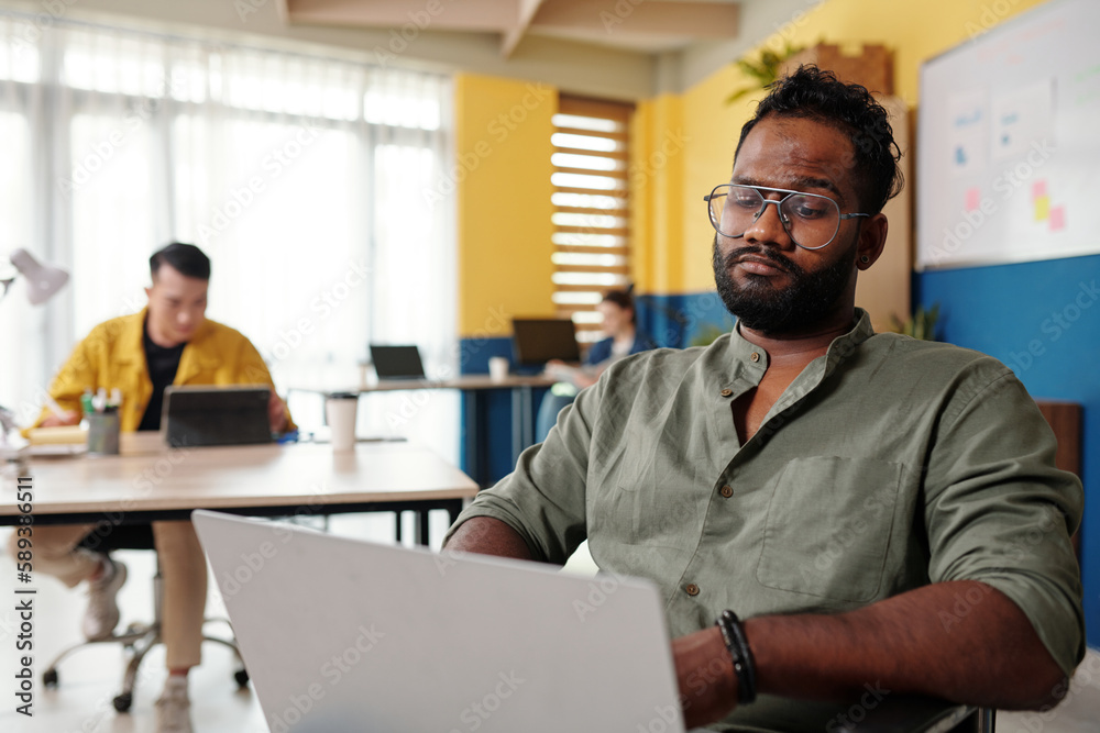 Fototapeta premium Frowning businessman in wheelchair working on laptop in office