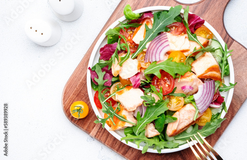 fresh salad with grilled salmon with tomato, cucumber, arugula, radicchio, red onion and lettuce with lemon oil dressing. Healthy delicious lunch. White table background, top view