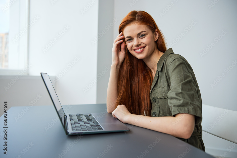portrait of a cute, smiling red-haired woman sitting at a laptop in a bright room portrait of a cute, smiling red-haired woman sitting at a laptop in a bright room