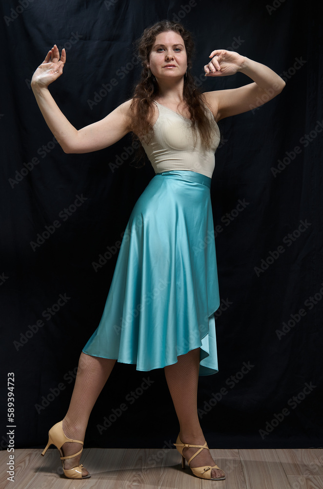 Naklejka premium Dancing woman in a blue skirt posing against a black background. Full length portrait