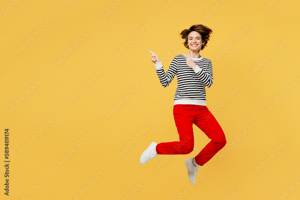 Full body fun young woman wear casual black and white shirt jump high point index finger aside indicate on workspace area copy space mock up isolated on plain yellow color background studio portrait. Full body fun young woman wear casual black and white shirt jump high point index finger aside indicate on workspace area copy space mock up isolated on plain yellow color background studio portrait.