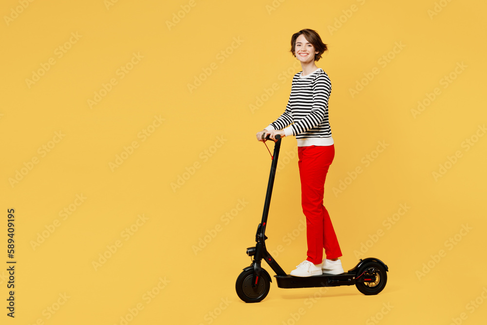 Full body young smiling happy cheerful active woman wear casual black and white shirt riding electric scooter look camera isolated on plain yellow color background studio portrait. Lifestyle concept. Full body young smiling happy cheerful active woman wear casual black and white shirt riding electric scooter look camera isolated on plain yellow color background studio portrait. Lifestyle concept.