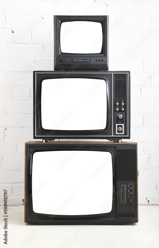 Three old televisions with white screens against a background of white bricks.