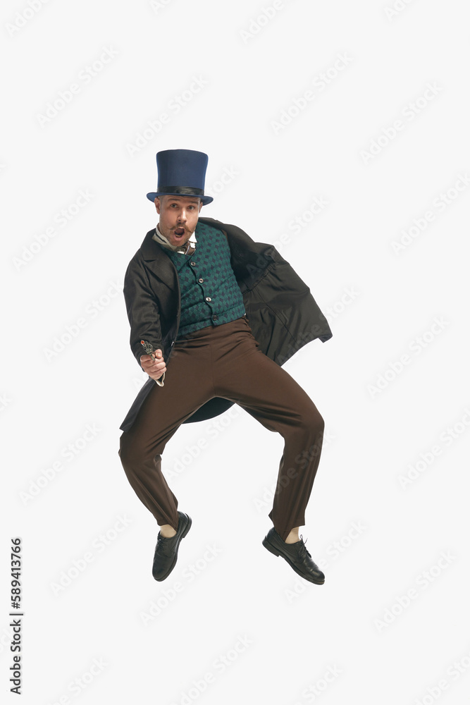 One man wearing vintage clothes, cylinder hat holding fake gun and jumping over white studio background. Dangerous guy