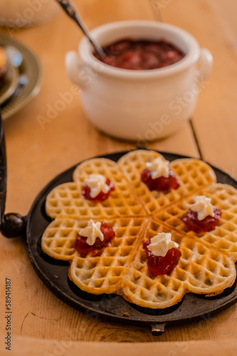An antique waffle iron with a freshly baked waffle and a dish with freshly baked waffles