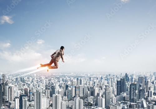 Businessman in suit and aviator hat flying in sky