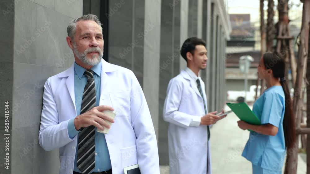 Slow motion VDO. Cheerful caucasian senior man doctor standing outdoor and drink coffee and smiling looking at camera. healthcare and medicine Slow motion VDO. Cheerful caucasian senior man doctor standing outdoor and drink coffee and smiling looking at camera. healthcare and medicine