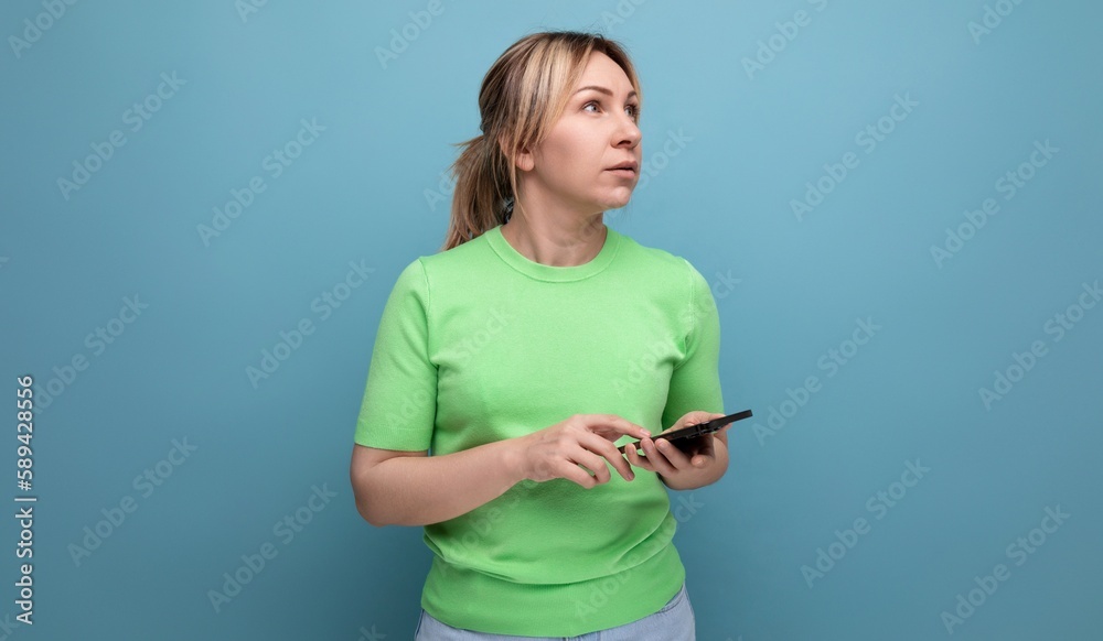 attractive blond girl meditates holding a smartphone in her hand on a blue background with copy space attractive blond girl meditates holding a smartphone in her hand on a blue background with copy space