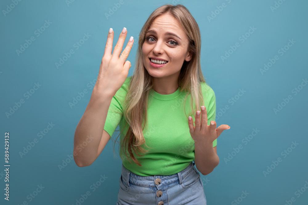 close-up photo of a blonde young woman in a casual outfit showing three fingers on a blue background close-up photo of a blonde young woman in a casual outfit showing three fingers on a blue background