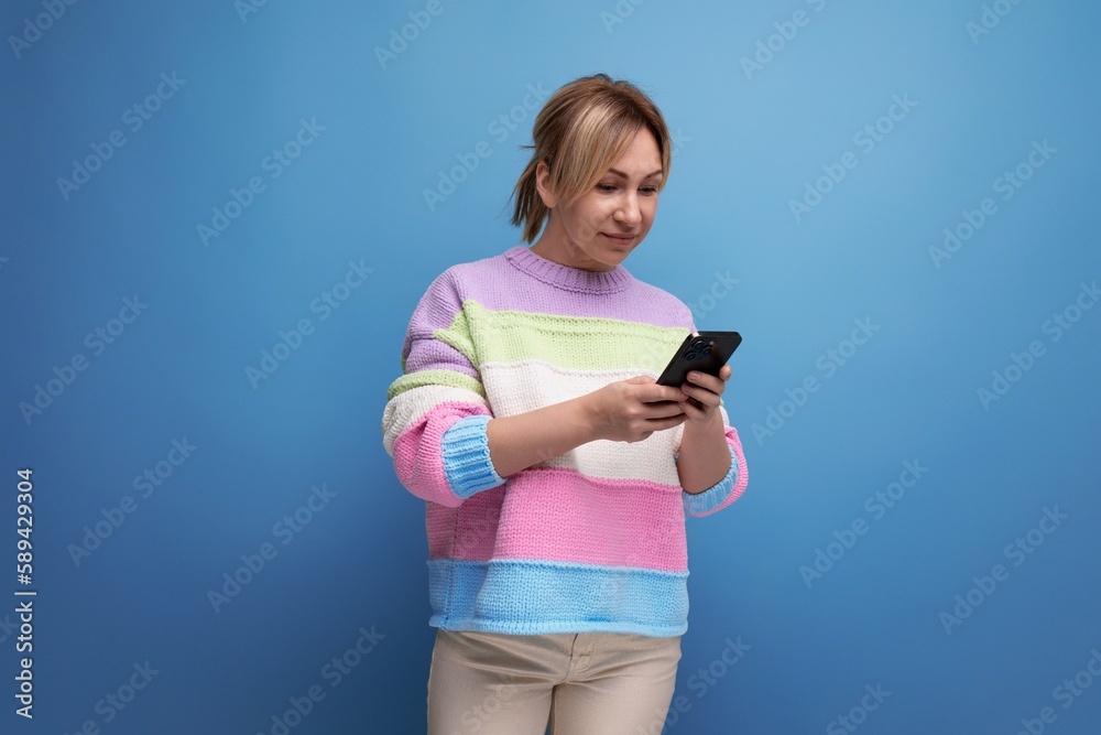 cute charming blond young woman in a striped sweater chatting in a smartphone on a blue background cute charming blond young woman in a striped sweater chatting in a smartphone on a blue background